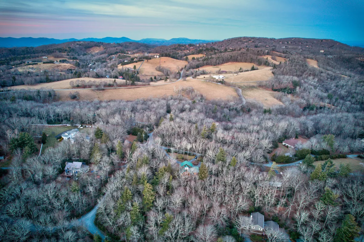 This view showcases rolling hills covered in dense trees with occasional homes dotting the landscape. The peaceful mood and wide perspective invite thoughts of tranquil strolls, nature watching, and family adventures in the great outdoors.
