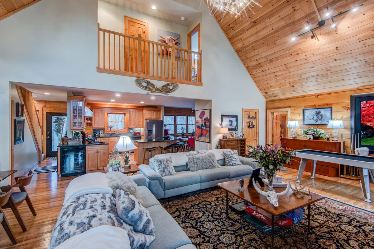 A spacious interior scene featuring a sofa with decorative cushions, a wooden dining table under a chandelier, and a pool table. The room radiates warmth and is designed for multiple activities, including family meals, game nights, and socializing.