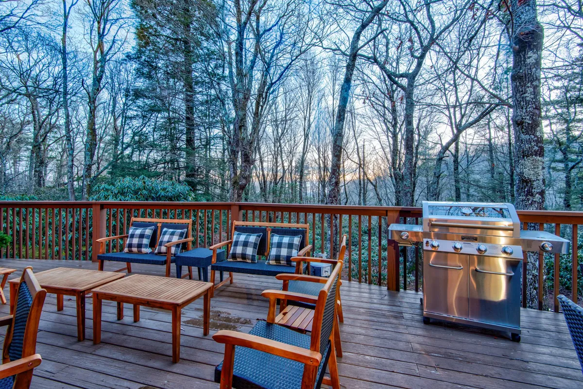 A wooden deck outfitted with a gas grill, outdoor seating, and views of surrounding trees. The space is ideal for barbecues, alfresco meals, and relaxing while soaking in the natural setting.