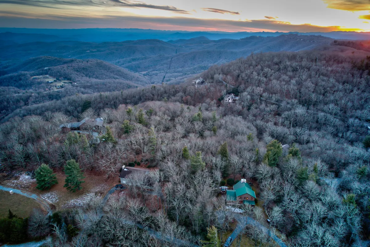A panoramic view of a mountainous landscape with scattered houses and dense tree cover, this image highlights the expansive Blue Ridge scenery. The vantage point suggests adventure and exploration, inviting visitors to discover hiking trails and breathtaking vistas.