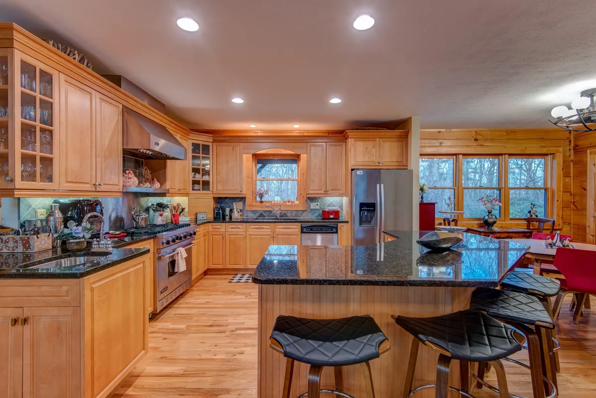 This kitchen scene highlights gorgeous granite countertops, handsome wooden cabinetry, a central island for prepping or socializing, and sleek stainless steel appliances. Ample natural light pours in through large windows, creating an inviting atmosphere for culinary creativity.